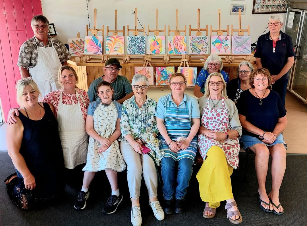 A group posing in front of their paintings following a group session